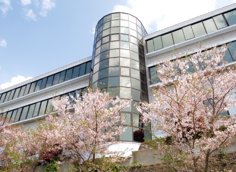 桜の開花時期に撮影された介護施設の建物外観。円形の塔と直線的な構造が特徴的。